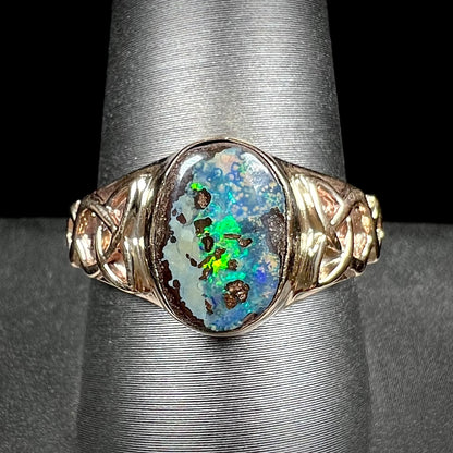 A unisex Celtic style natural boulder opal ring cast in yellow gold.  The opal shines green and blue.