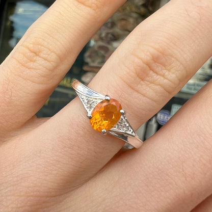 A sterling silver ladies' ring set with a faceted oval cut Mexican fire opal and round white zircon accent stones.