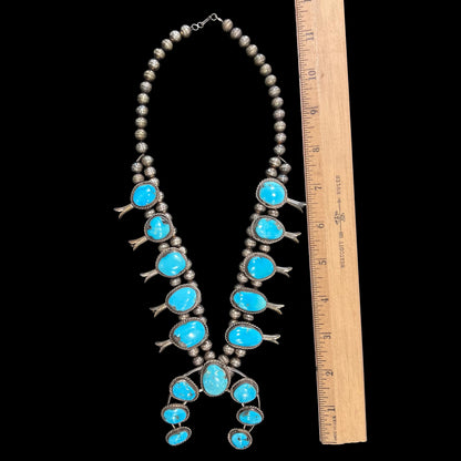 A sterling silver, Navajo style squash blossom necklace set with Morenci turquoise stones.  The legnth is designed for women and children.