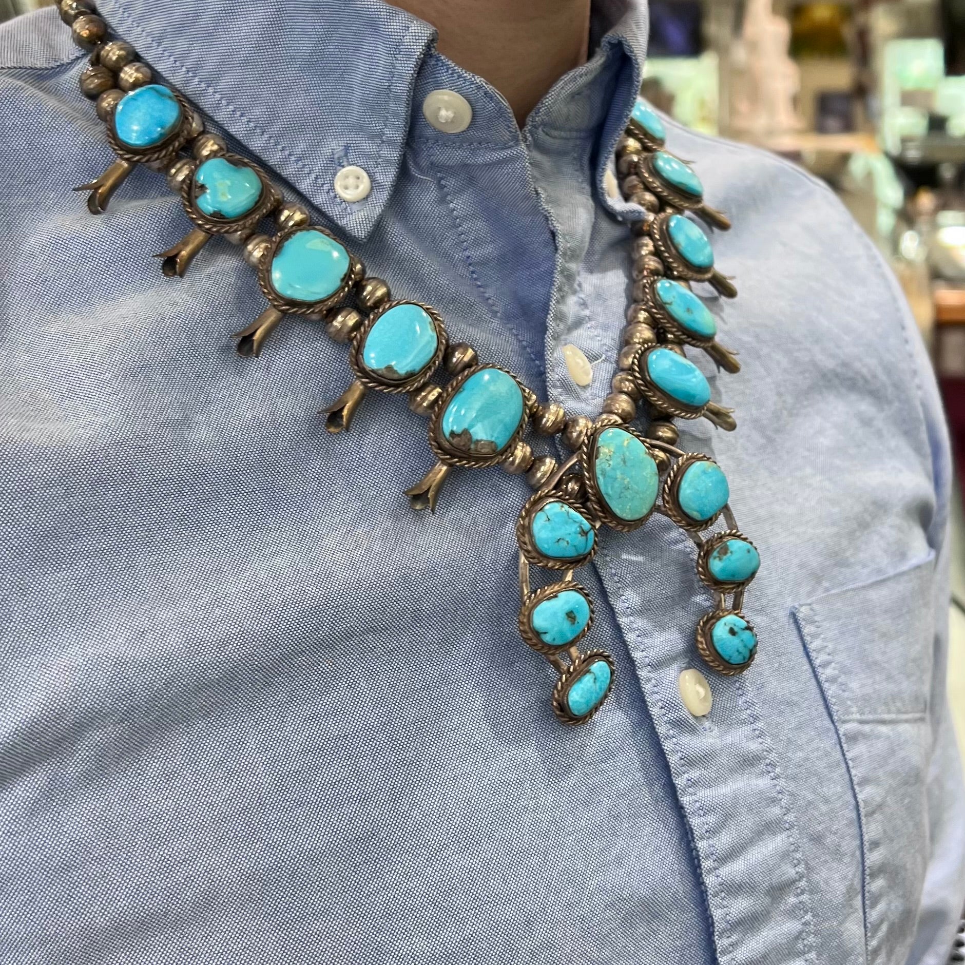 A sterling silver, Navajo style squash blossom necklace set with Morenci turquoise stones.  The legnth is designed for women and children.