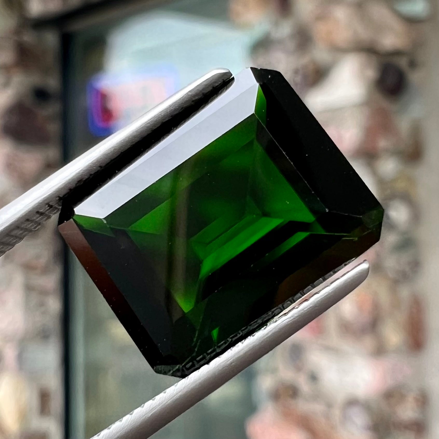 A large, emerald cut chrome diopside gemstone.  The gem is dark green color.