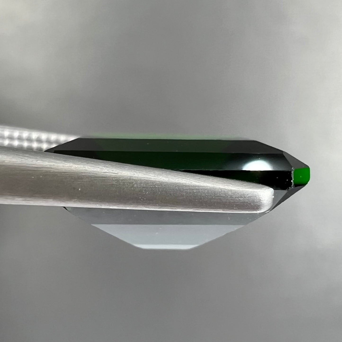 A large, emerald cut chrome diopside gemstone.  The gem is dark green color.
