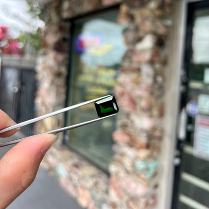 A large, emerald cut chrome diopside gemstone.  The gem is dark green color.