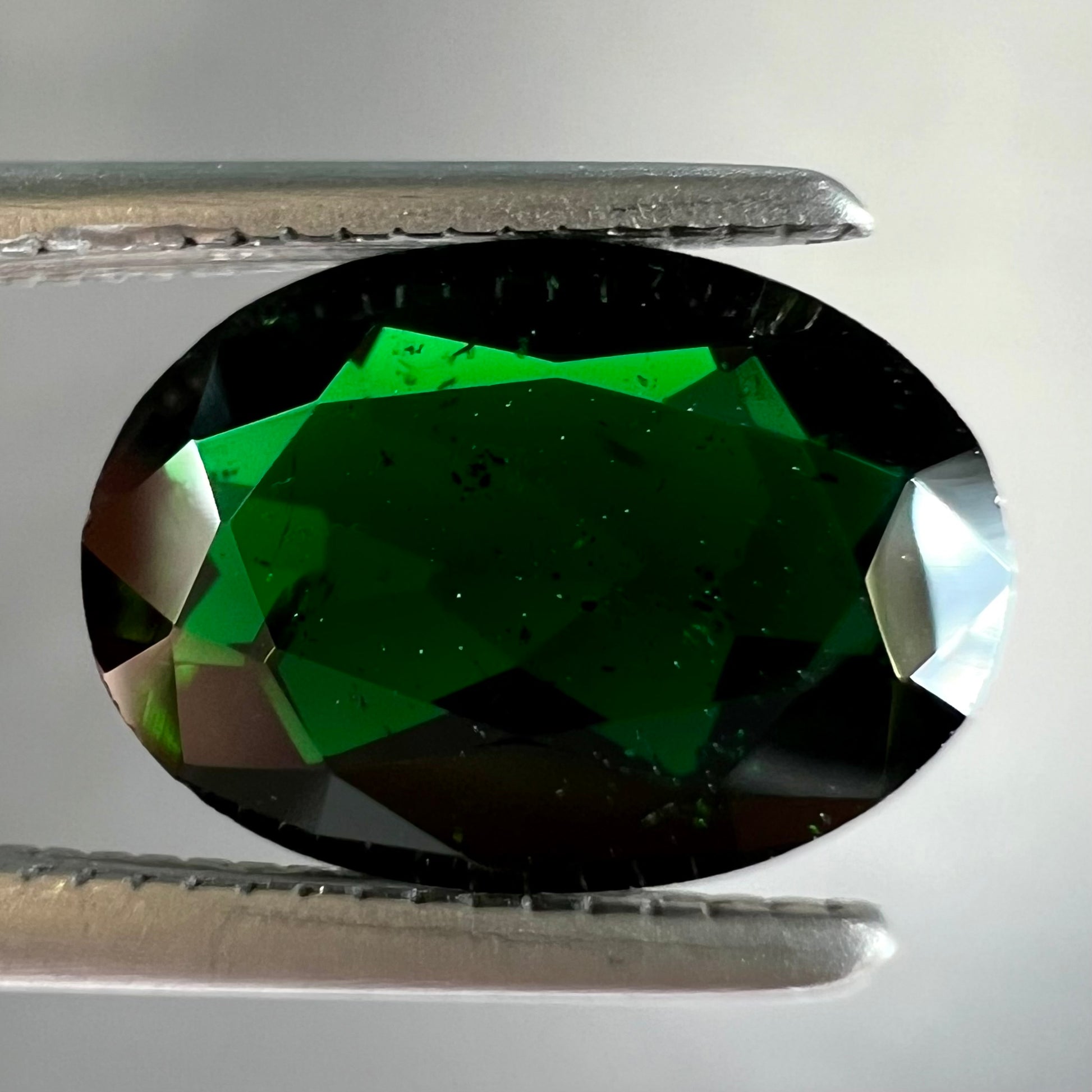 A faceted oval cut chrome tourmaline gemstone.  The stone is dark green.