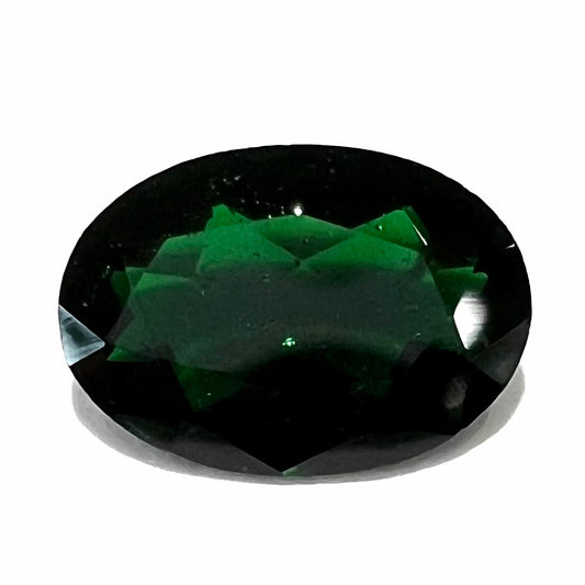 A faceted oval cut chrome tourmaline gemstone.  The stone is dark green.