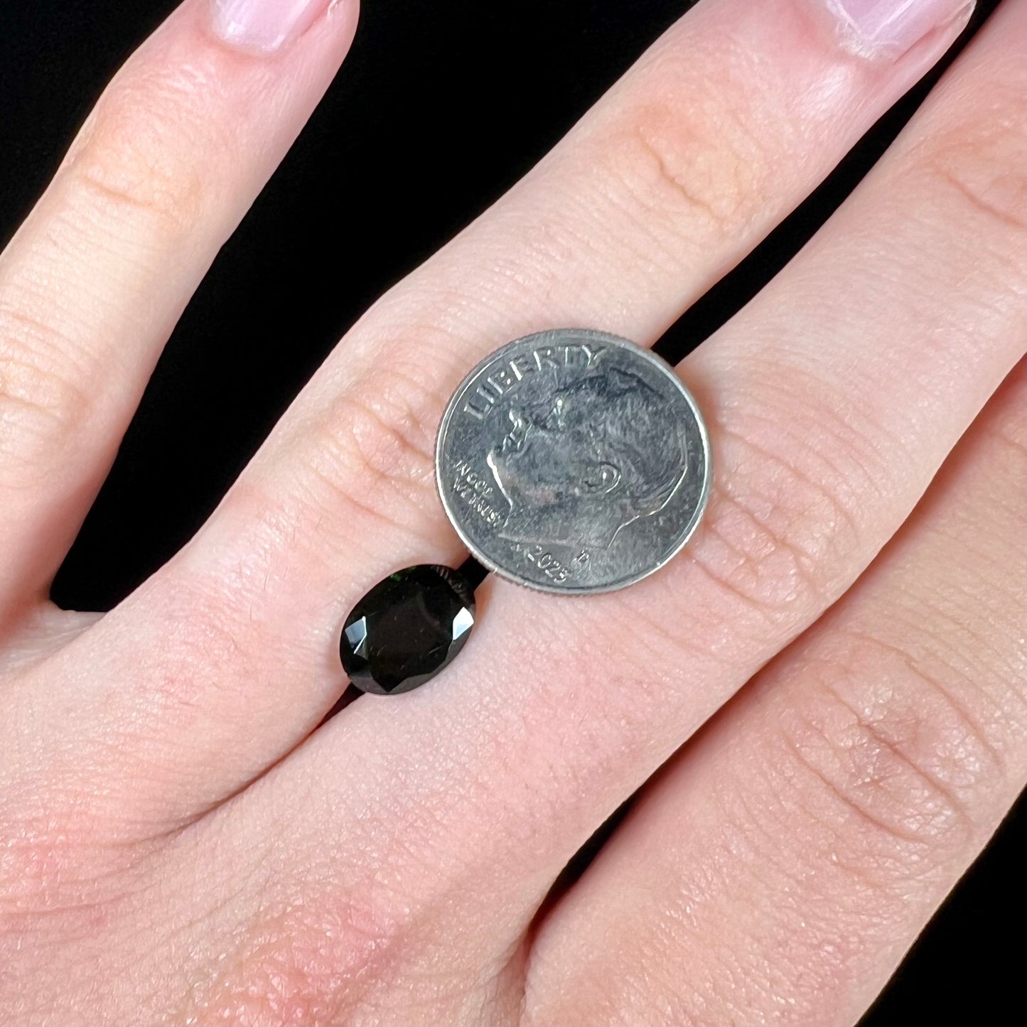 A faceted oval cut chrome tourmaline gemstone.  The stone is dark green.