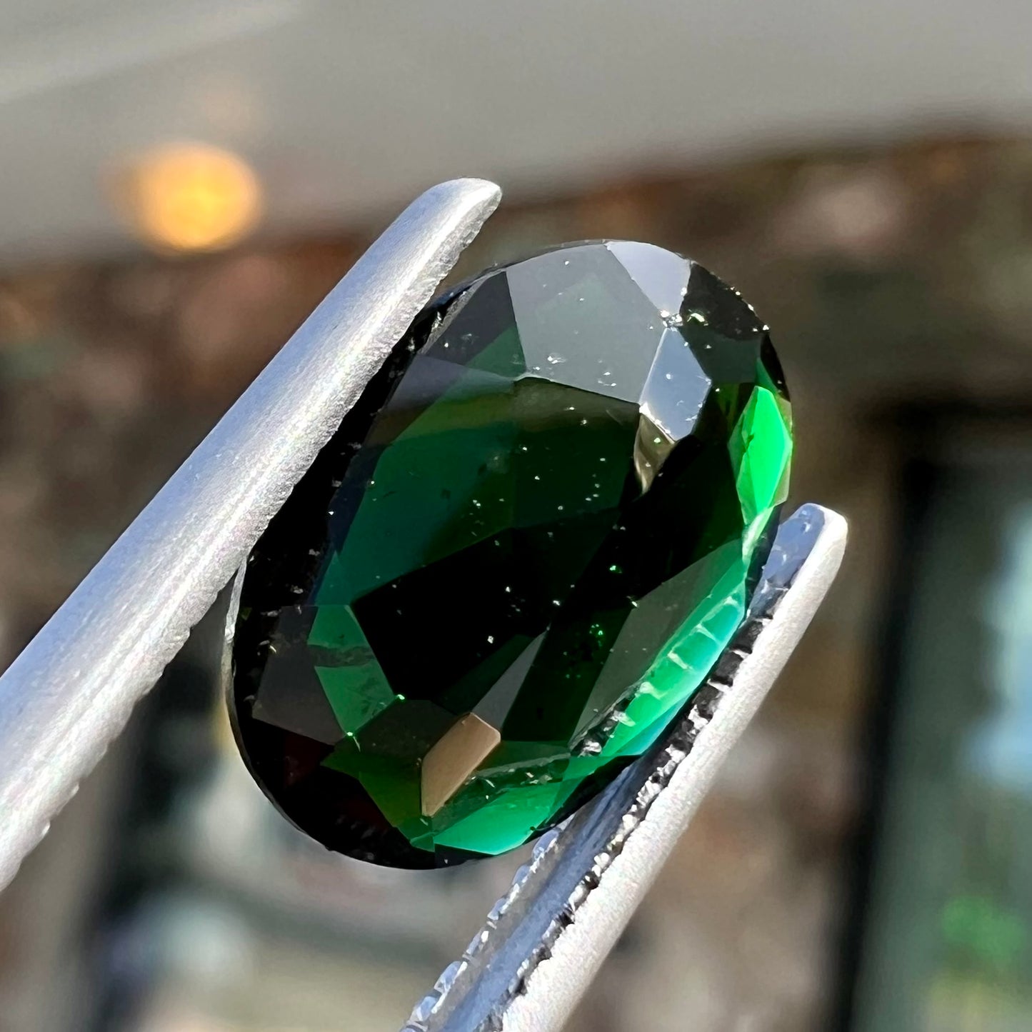 A faceted oval cut chrome tourmaline gemstone.  The stone is dark green.