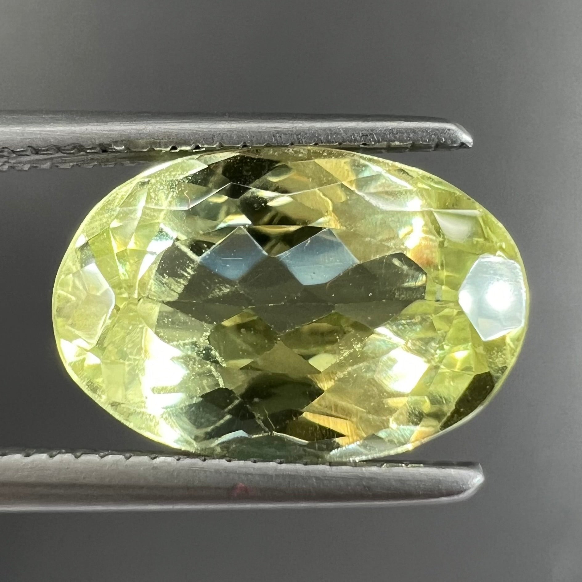 A loose, faceted oval cut chrysoberyl gemstone.  The stone is a greenish yellow color.