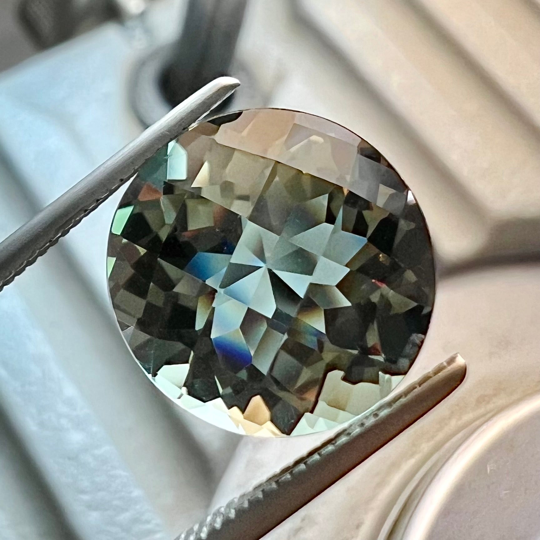 A loose, round brilliant checkerboard cut Zandrite gemstone.  The stone changes colors from greenish tan to purple.
