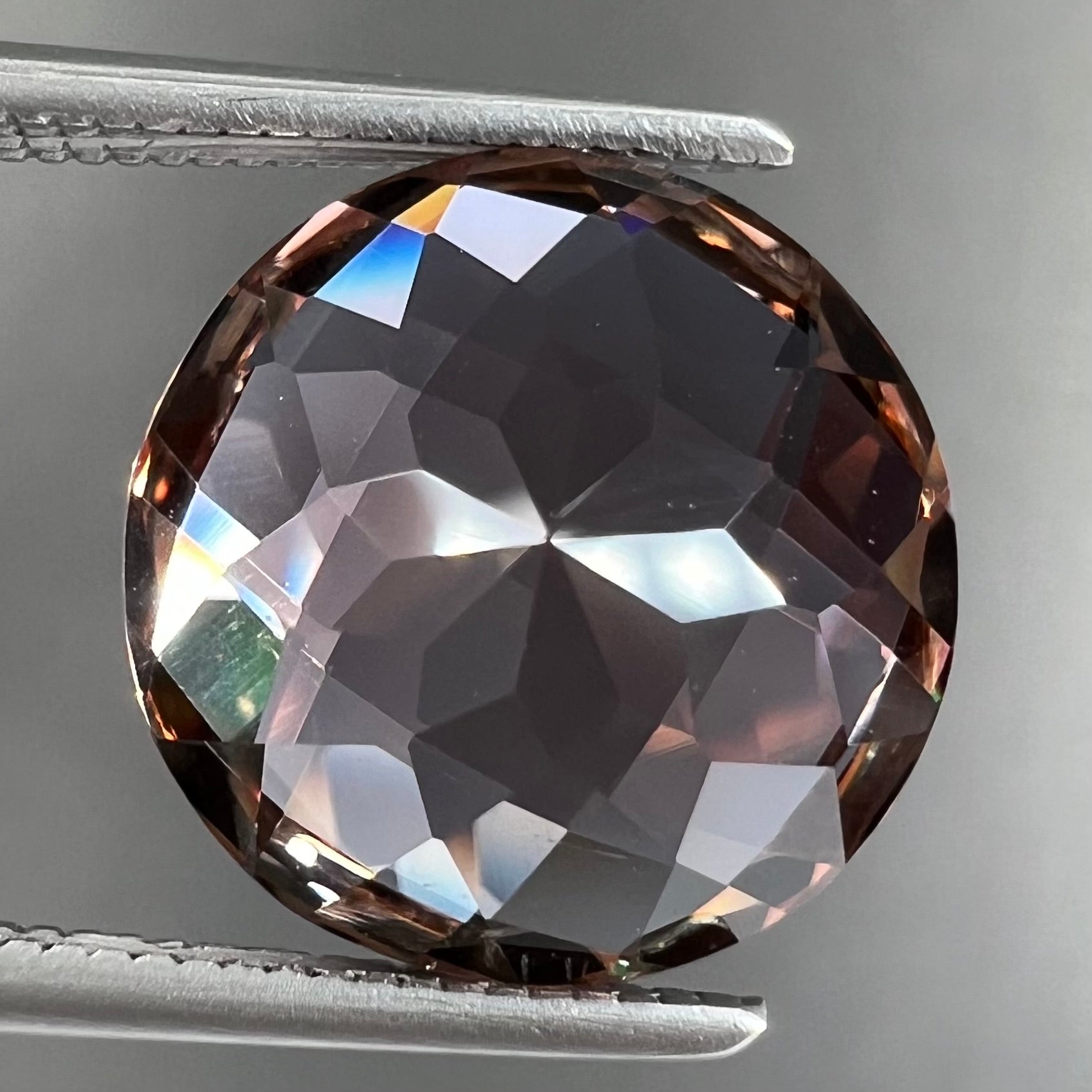 A loose, round brilliant checkerboard cut Zandrite gemstone.  The stone changes colors from greenish tan to purple.