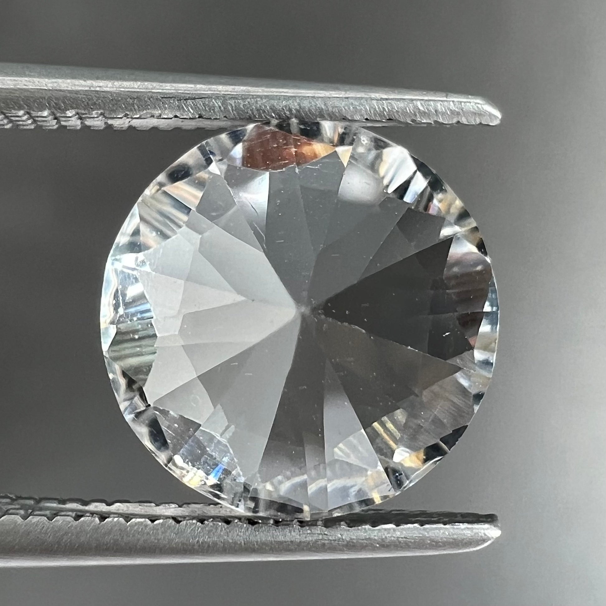 A round brilliant cut petalite gemstone.  The stone is colorless.