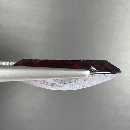 A loose, marquise cut cuprite gemstone.  The stone is a deep, crimson red color.