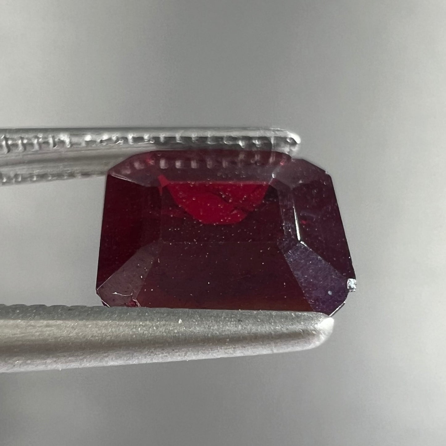 A loose, modified Asscher cut cuprite gemstone.  The stone is a deep, crimson red color and has several chips along the girdle.