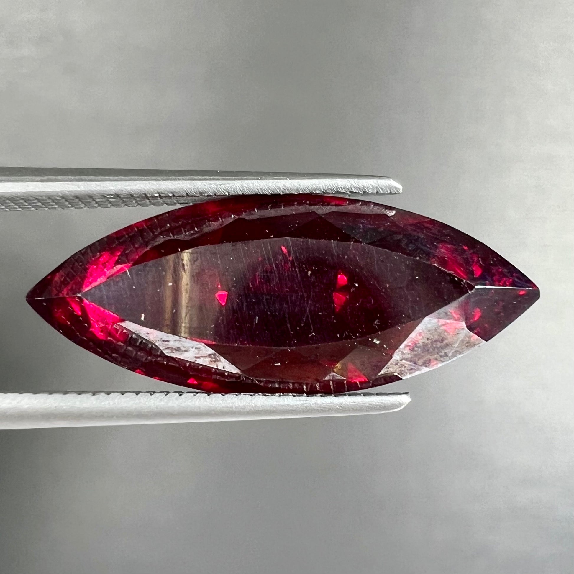 A loose, marquise cut cuprite gemstone.  The stone is a deep, crimson red color.