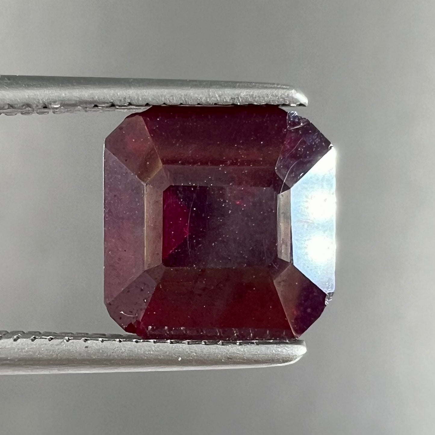 A loose, modified Asscher cut cuprite gemstone.  The stone is a deep, crimson red color and has several chips along the girdle.