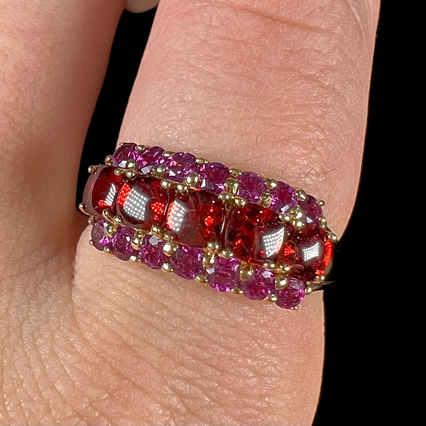 A gold ring set with buff cut cushion shaped almandine garnets with round cut purple rhodolite garnet accents.