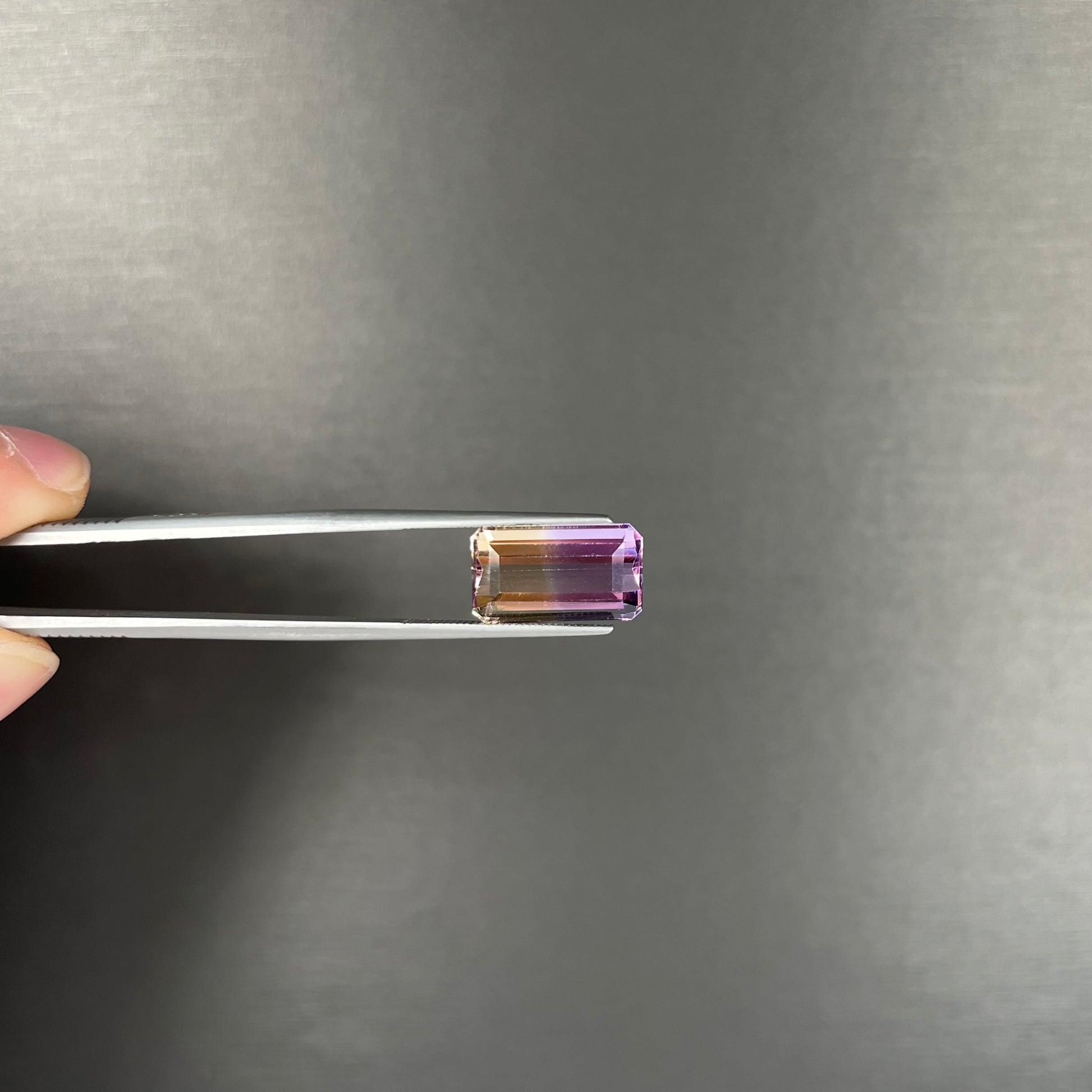 A loose, emerald cut ametrine stone.  The color fades from light purple to light yellow.
