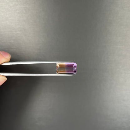 A loose, emerald cut ametrine stone.  The color fades from light purple to light yellow.