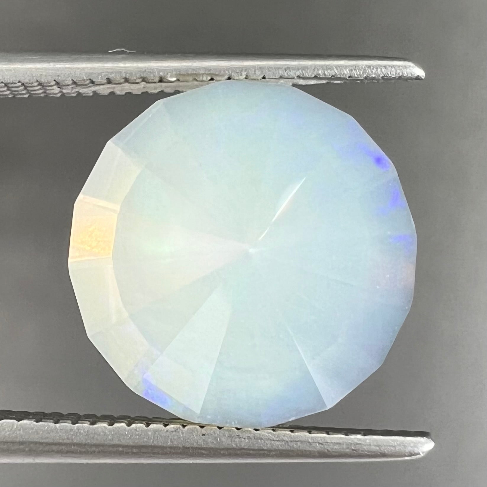 A loose, modified round cut Mexican fire opal gemstone.  The stone is transluscent light yellow with green and blue fire.