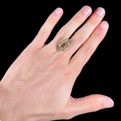 A faceted oval cut rutilated quartz gemstone.  The stone is smoky color with golden rutile needle inclusions.