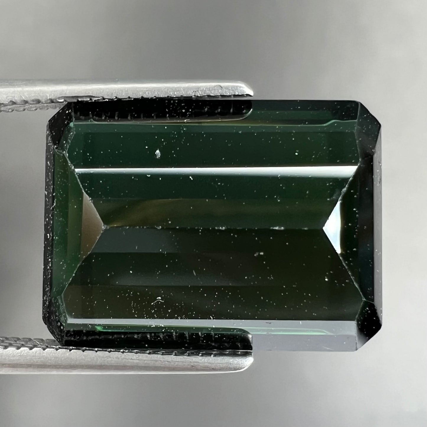 A faceted emerald cut dark green tourmaline gemstone.