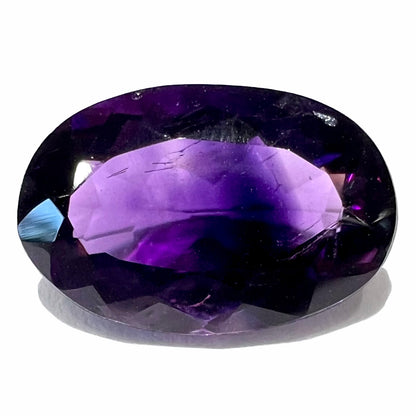 A loose, faceted oval cut Siberian amethyst gemstone.  The stone is purple color with blue and red flashes.  The amethyst weighs 5.25 carats.