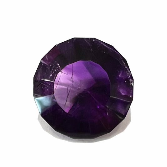 A modified round cut amethyst gemstone.  The stone is a dark bluish purple color.