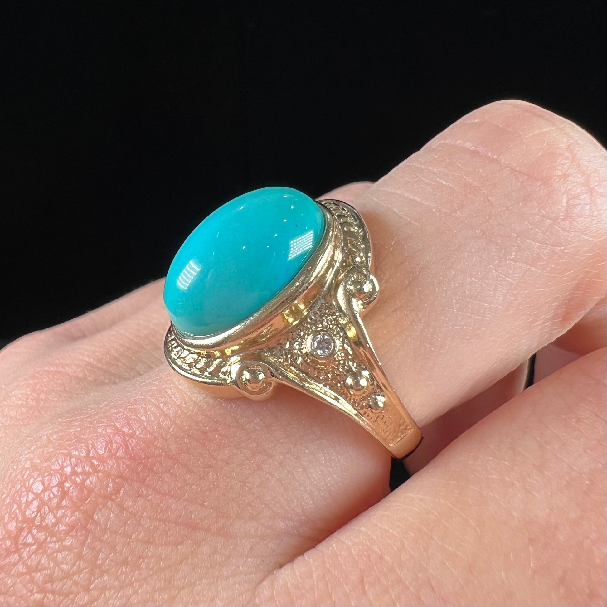 A yellow gold ring set with a greenish blue Sleeping Beauty turquoise cabochon with two diamond accents.