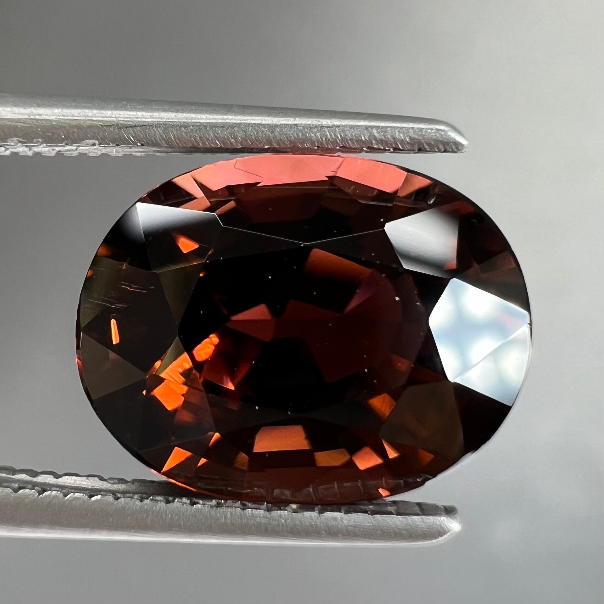 A loose, faceted oval cut dravite tourmaline gemstone.  The stone is a dark brown color with a purple secondary color.