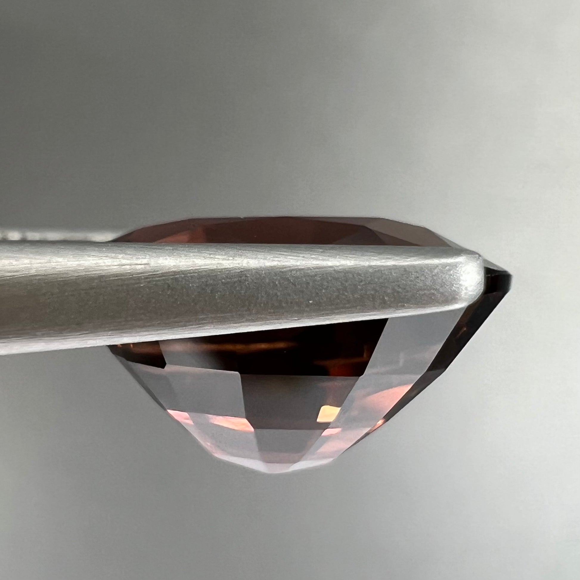 A loose, faceted oval cut dravite tourmaline gemstone.  The stone is a dark brown color with a purple secondary color.