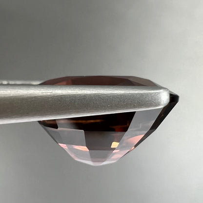 A loose, faceted oval cut dravite tourmaline gemstone.  The stone is a dark brown color with a purple secondary color.