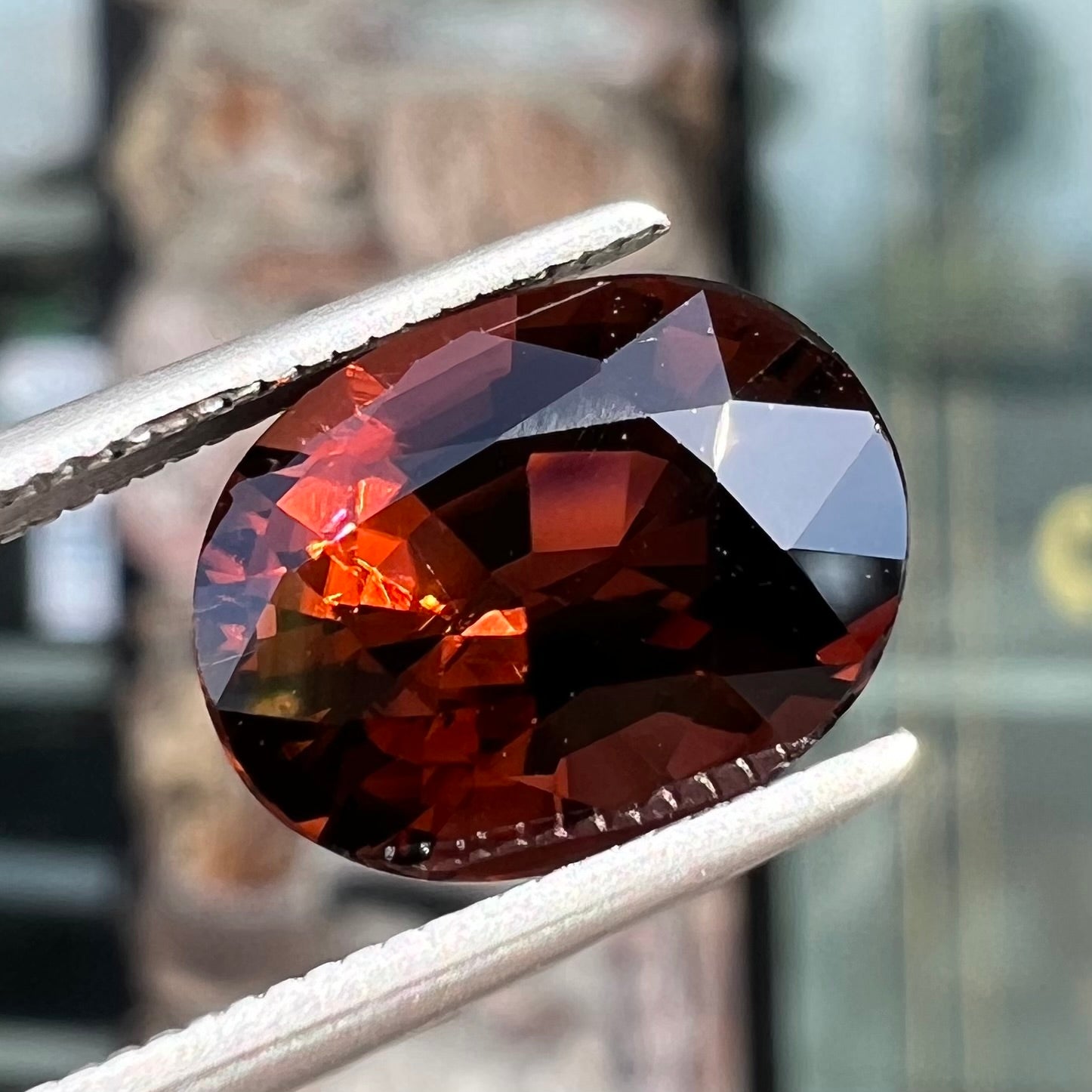 A loose, faceted oval cut dravite tourmaline gemstone.  The stone is a dark brown color with a purple secondary color.