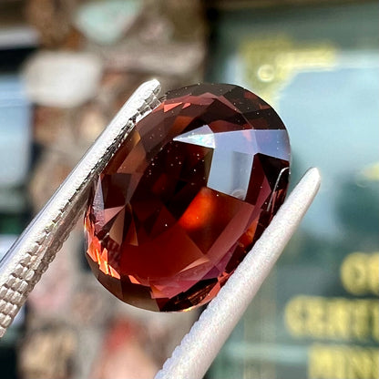 A loose, faceted oval cut dravite tourmaline gemstone.  The stone is a dark brown color with a purple secondary color.