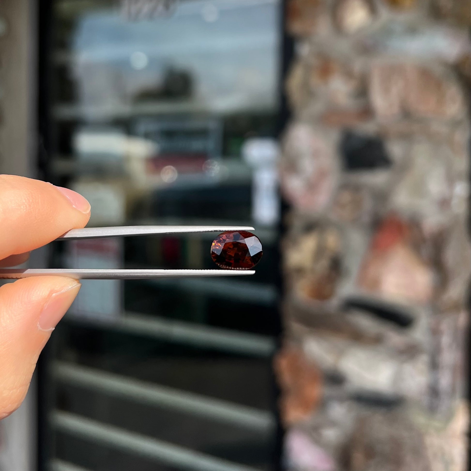 A loose, faceted oval cut dravite tourmaline gemstone.  The stone is a dark brown color with a purple secondary color.