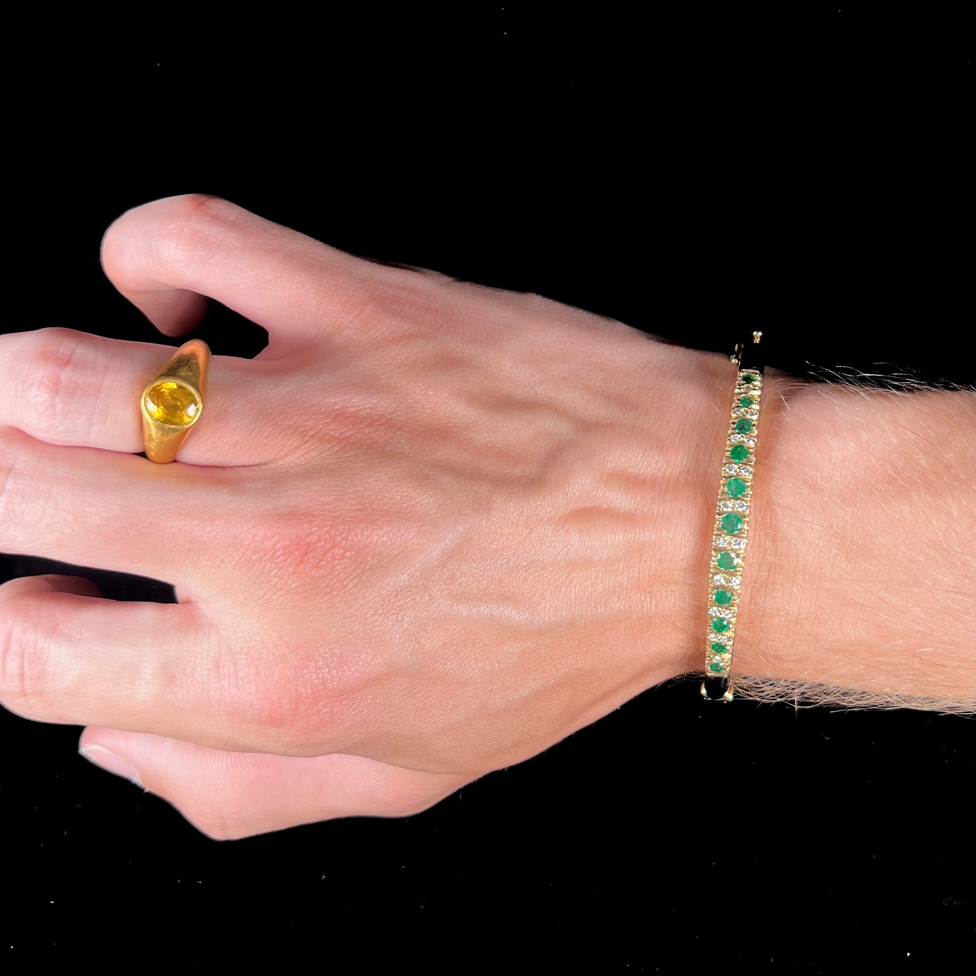 A ladies' yellow gold bangle bracelet set with round cut emeralds and diamonds.