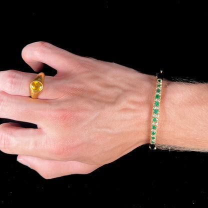 A ladies' yellow gold bangle bracelet set with round cut emeralds and diamonds.