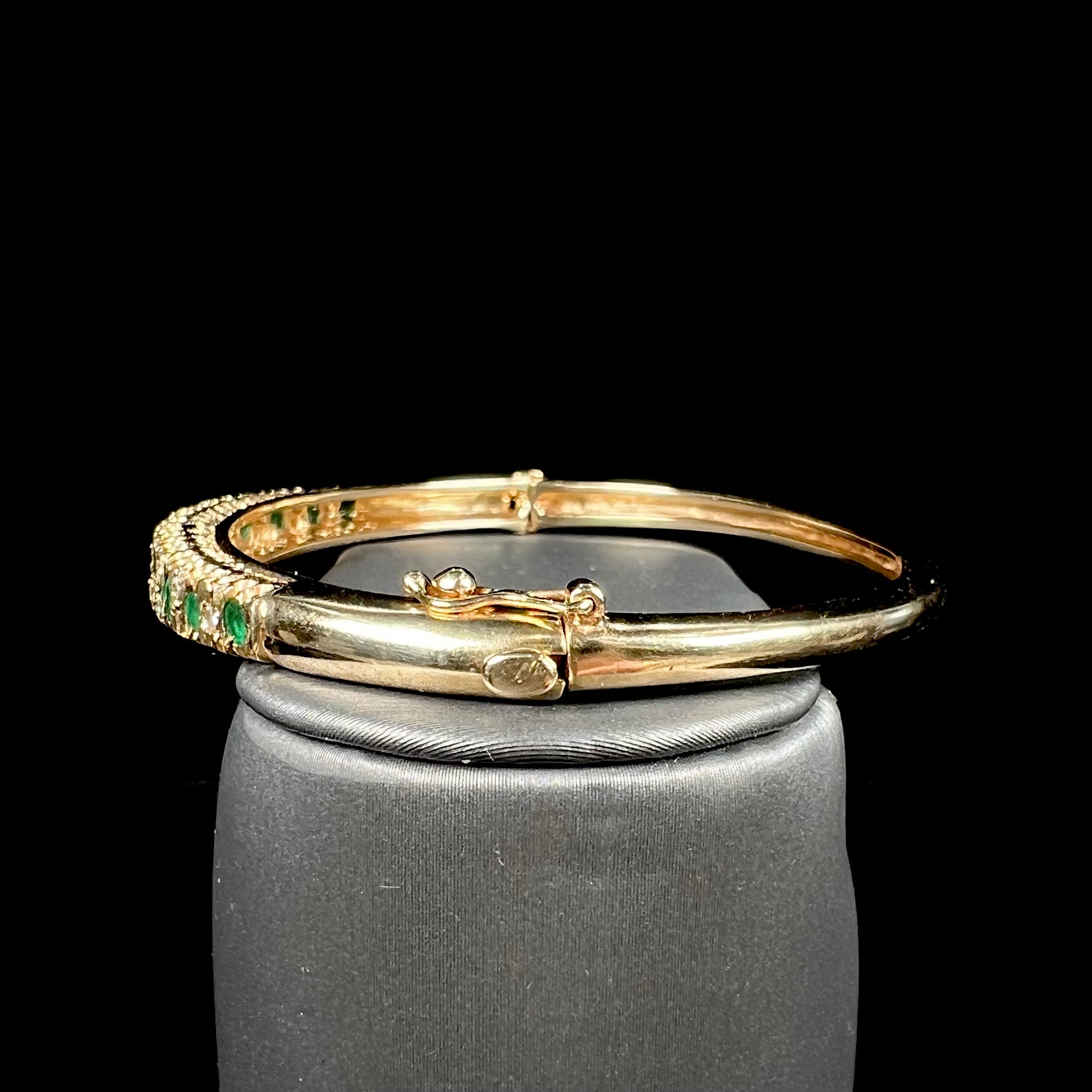 A ladies' yellow gold bangle bracelet set with round cut emeralds and diamonds.