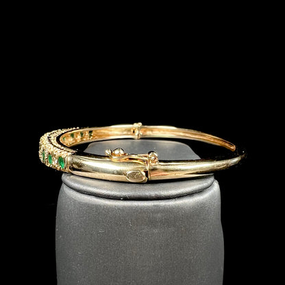 A ladies' yellow gold bangle bracelet set with round cut emeralds and diamonds.