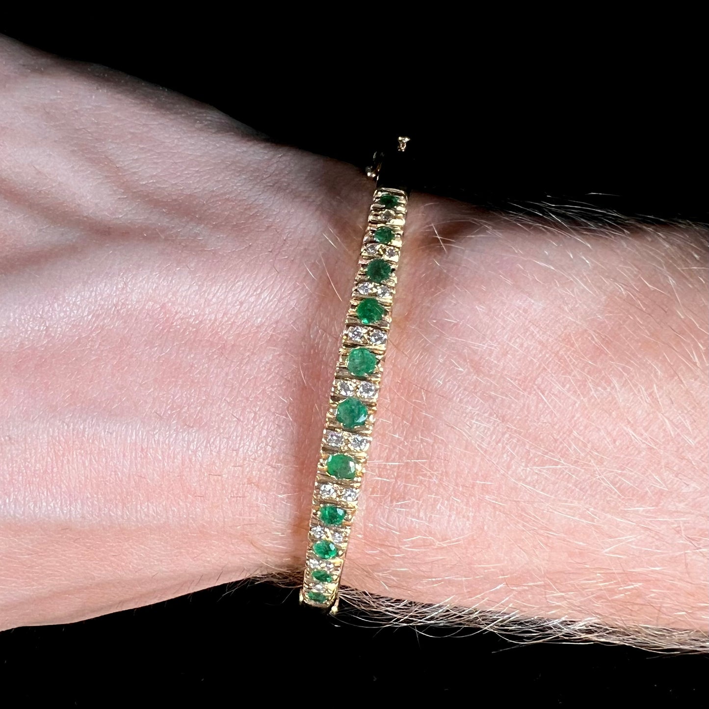 A ladies' yellow gold bangle bracelet set with round cut emeralds and diamonds.