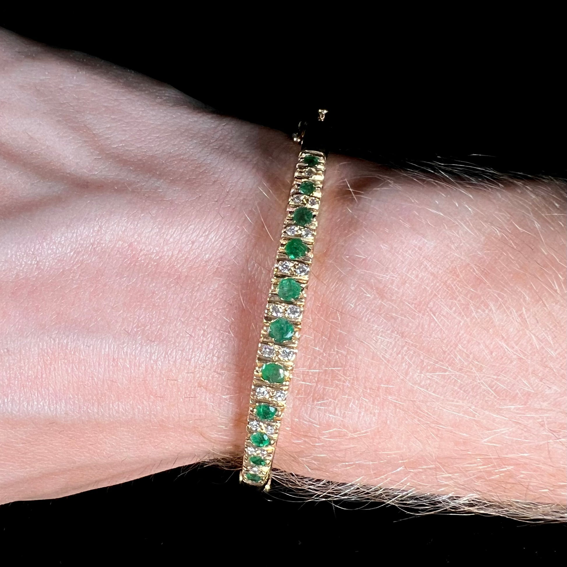 A ladies' yellow gold bangle bracelet set with round cut emeralds and diamonds.