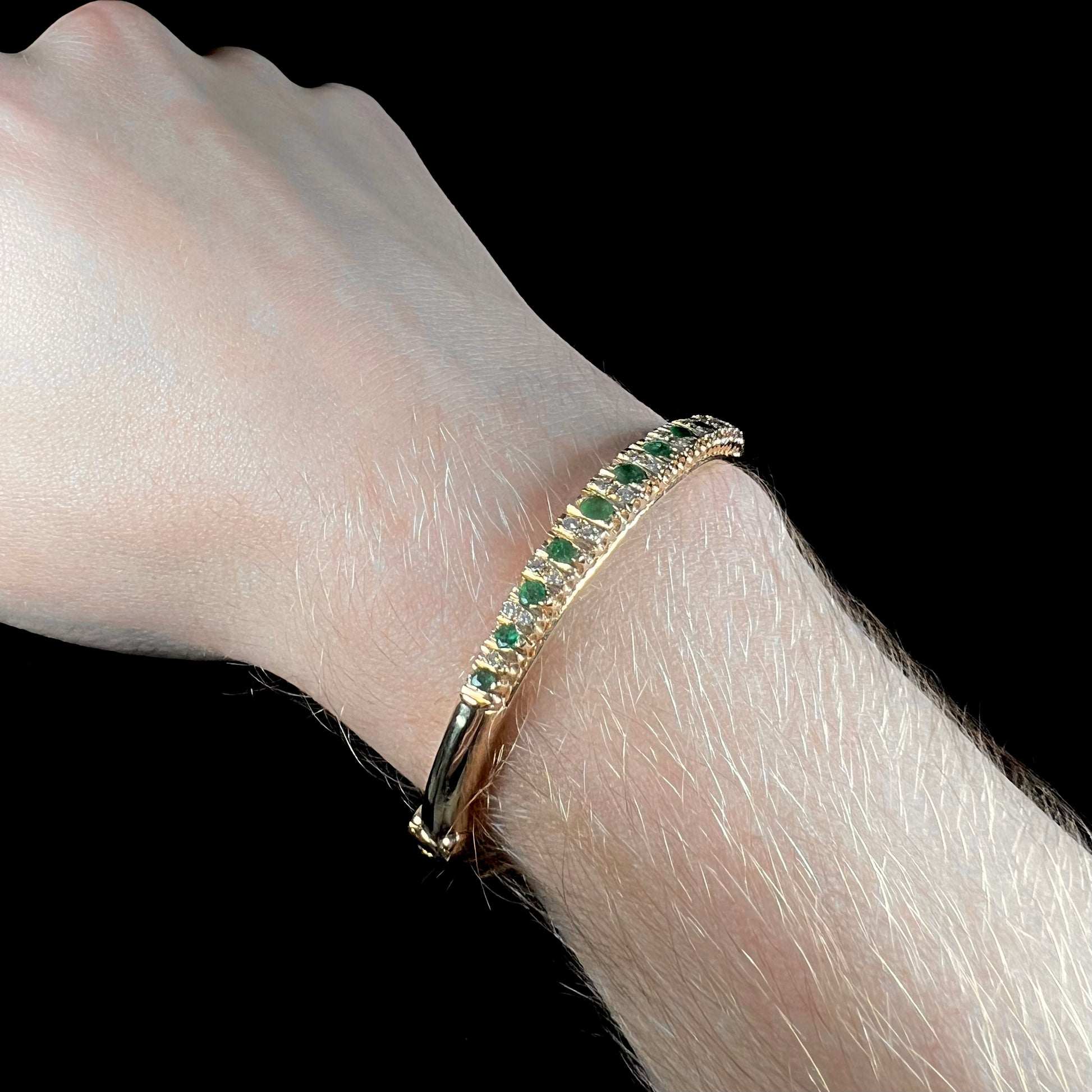 A ladies' yellow gold bangle bracelet set with round cut emeralds and diamonds.