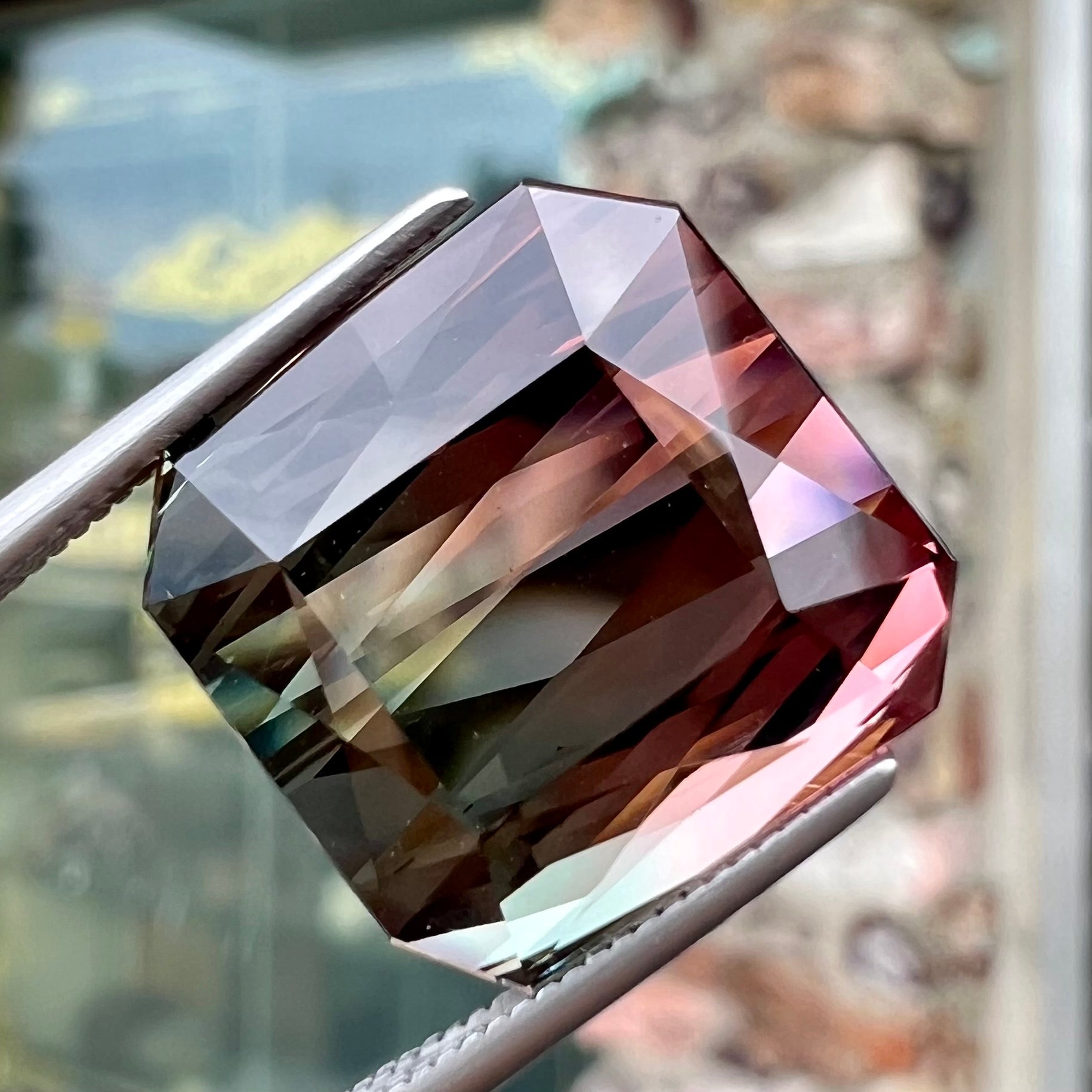 A loose, faceted modified emerald cut bicolor tourmaline gemstone.  The stone transitions from dark pink to dark green colors.