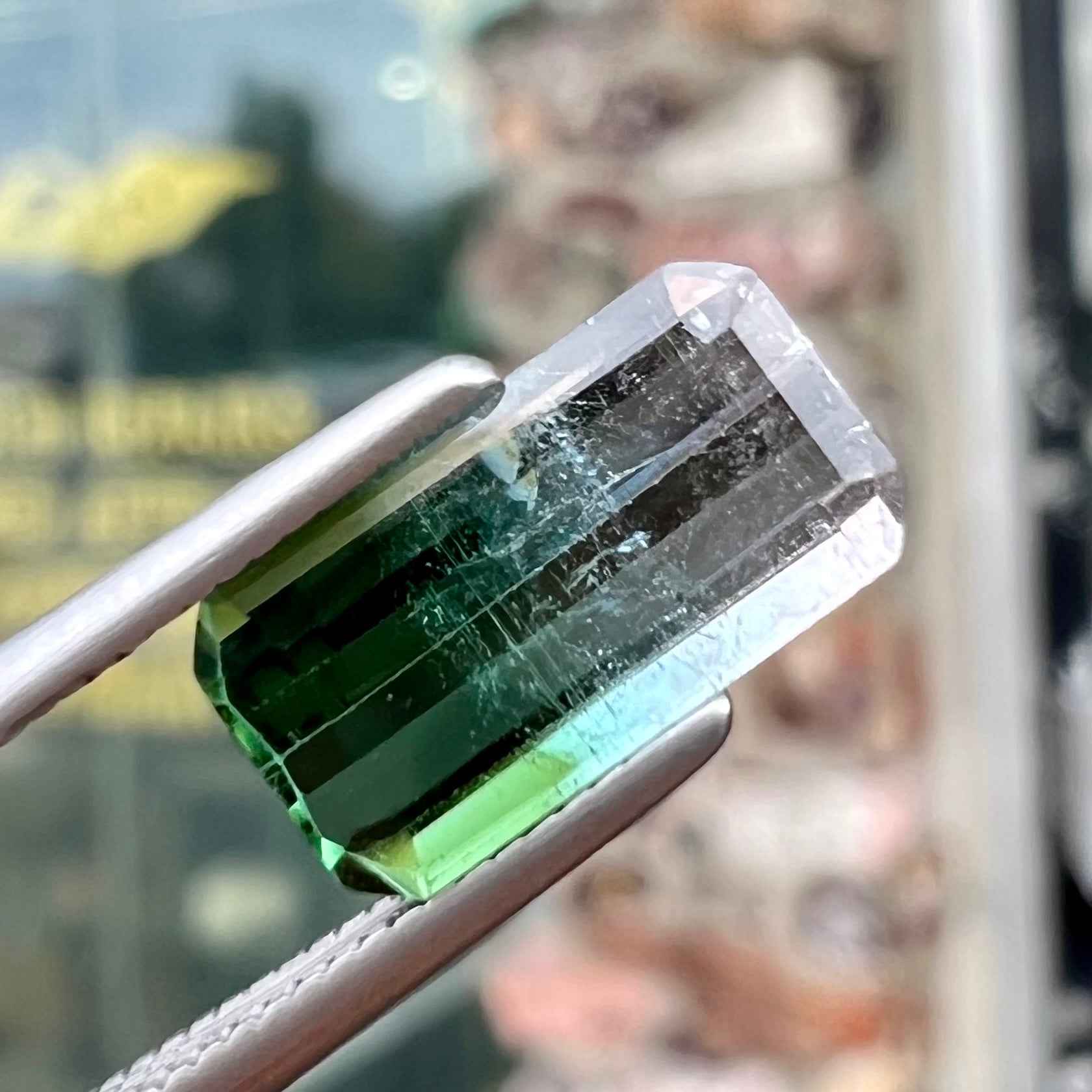 A loose, emerald cut tricolor tourmaline gemstone.  The stone transitions from green to blue to white colors.