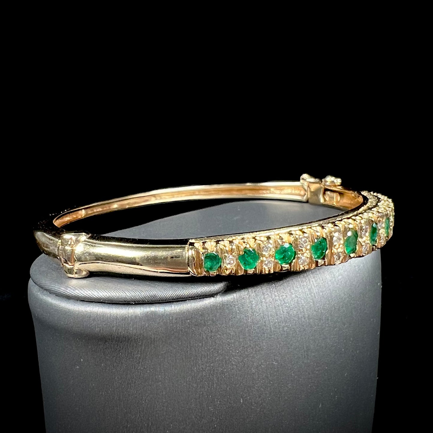 A ladies' yellow gold bangle bracelet set with round cut emeralds and diamonds.