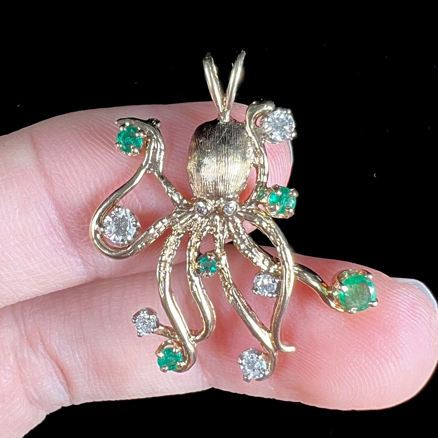 A yellow gold octopus pendant set with round cut emeralds and diamonds in the tentacles.