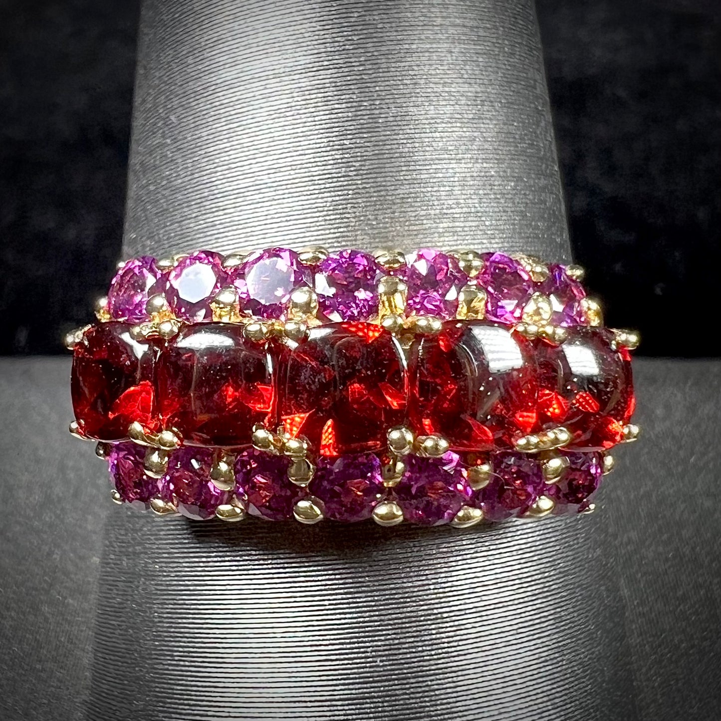 A gold ring set with buff cut cushion shaped almandine garnets with round cut purple rhodolite garnet accents.