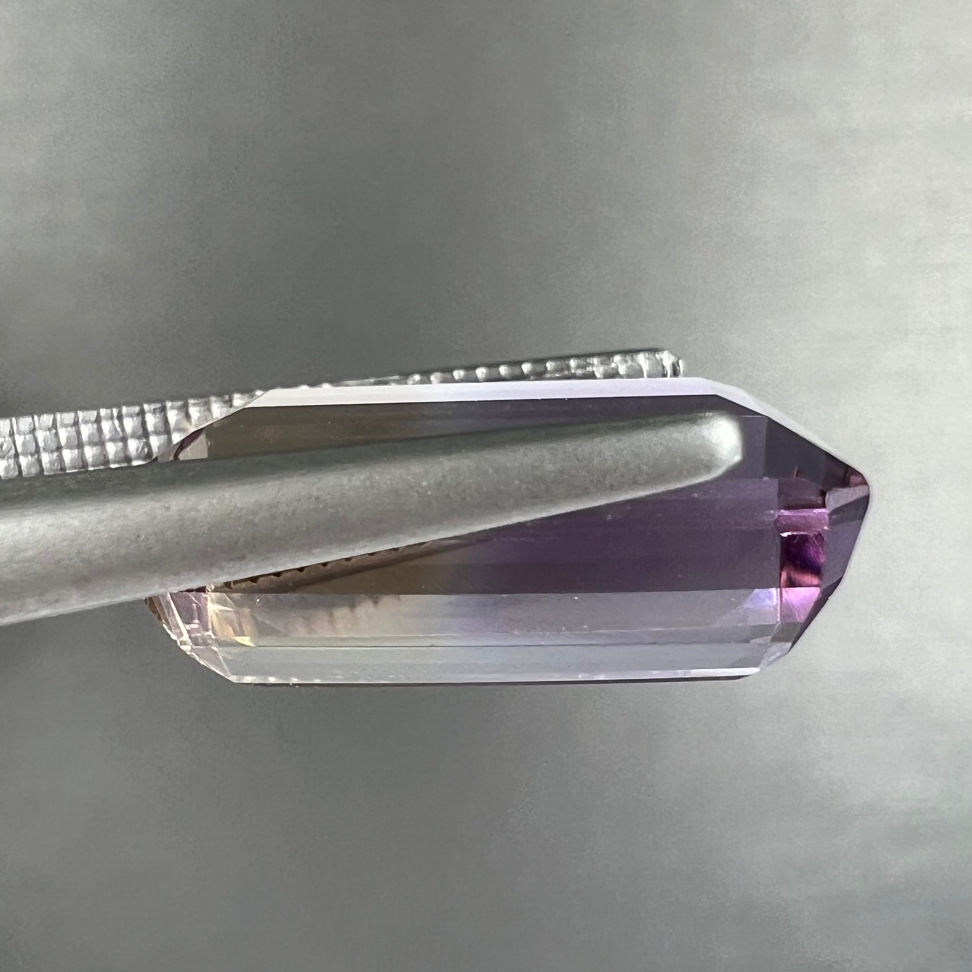 A loose, emerald cut ametrine stone.  The color fades from light purple to light yellow.