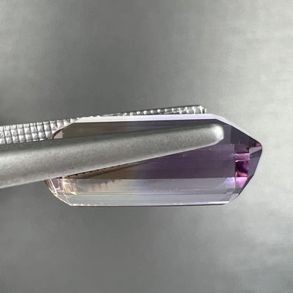 A loose, emerald cut ametrine stone.  The color fades from light purple to light yellow.