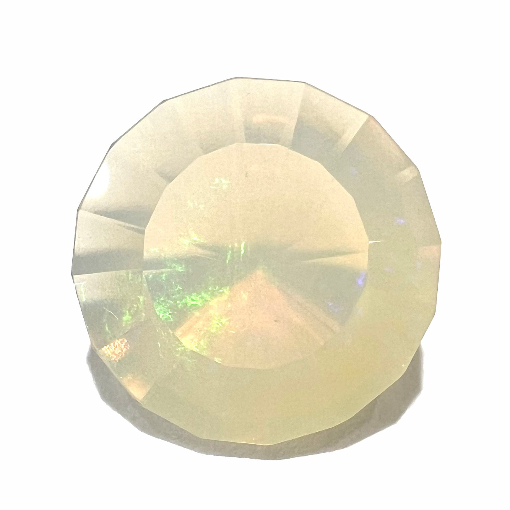 A loose, modified round cut Mexican fire opal gemstone.  The stone is transluscent light yellow with green and blue fire.