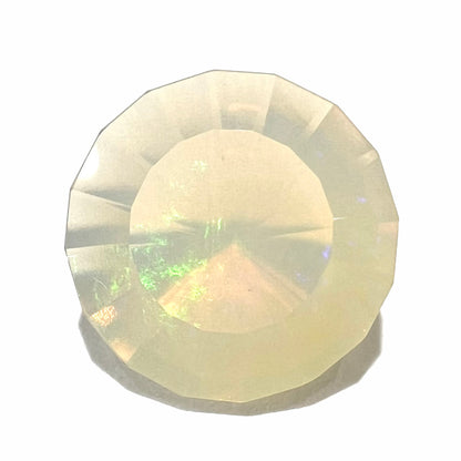 A loose, modified round cut Mexican fire opal gemstone.  The stone is transluscent light yellow with green and blue fire.